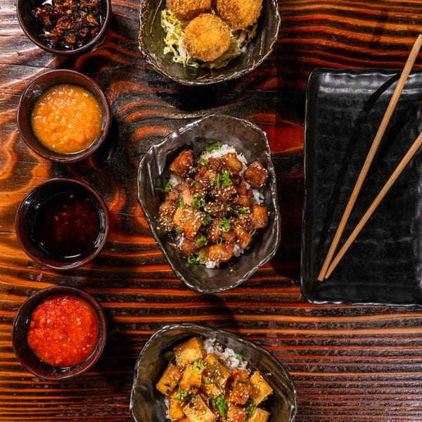 Top-down view of Baka Umai ramen dishes, including fried tofu, rice, sauces, and croquettes.