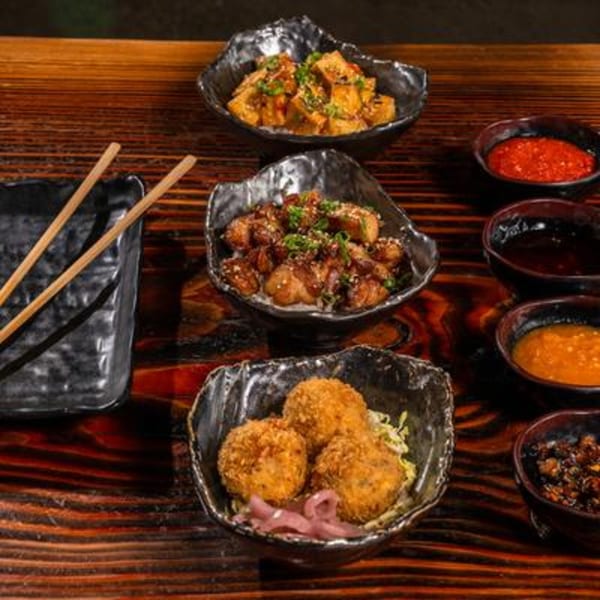 Assortment of Asian dishes including fried tofu, crispy pork belly, and croquettes with various dipping sauces.
