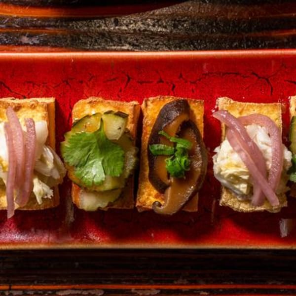 Four appetizers on a red rectangular plate, topped with various ingredients like mushrooms and pickled onions.