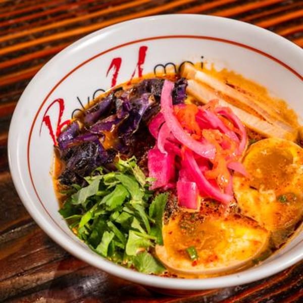 A vibrant bowl of ramen with purple cabbage, pickled red onions, cilantro, and two soft-boiled eggs.