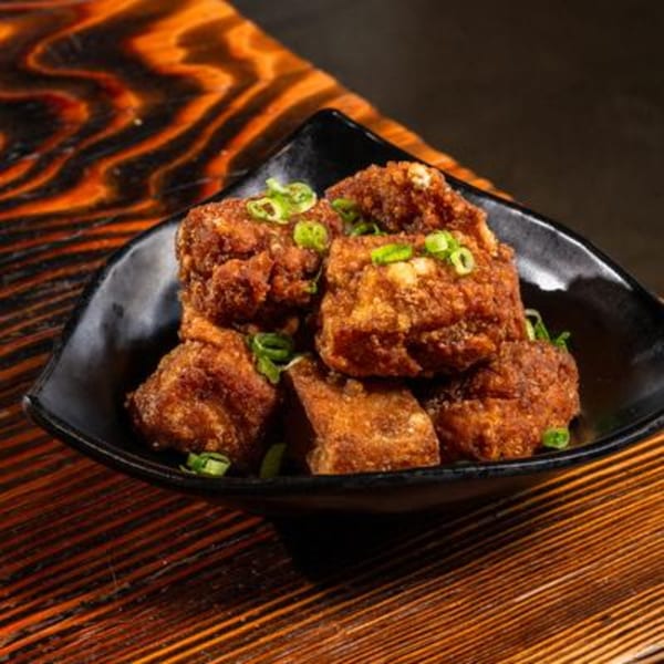 Crispy fried chicken pieces, garnished with green onions, served in a black bowl on a wooden table.