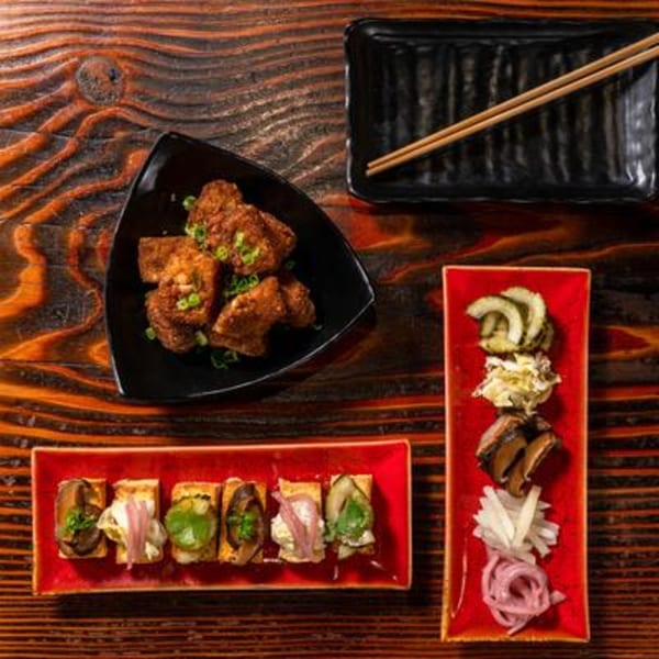 Assortment of Japanese appetizers, including fried chicken, pickled vegetables, and tofu bites on a wooden table.