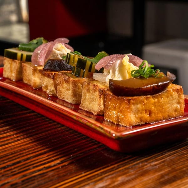 Fried tofu squares topped with various garnishes, including pickled onions, cucumber, and a dark sauce.