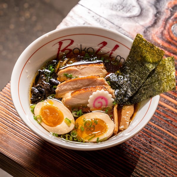 Baka Umai ramen bowl with chicken, soft-boiled eggs, nori, and scallions on a wooden table.