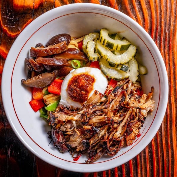 A Baka Umai ramen bowl with pulled pork, mushrooms, pickled cucumbers, and a poached egg.