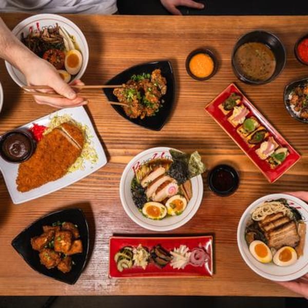 Overhead view of a wooden table laden with various Japanese dishes, including ramen, katsu, and appetizers.