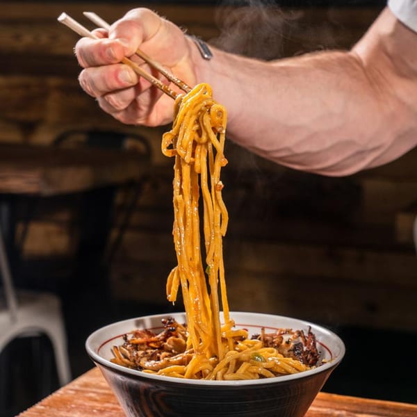A hand uses chopsticks to lift steaming, saucy ramen noodles from a bowl at Baka Umai.