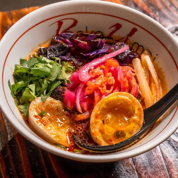 A bowl of Baka Umai ramen with eggs, purple cabbage, pickled onions, and cilantro.